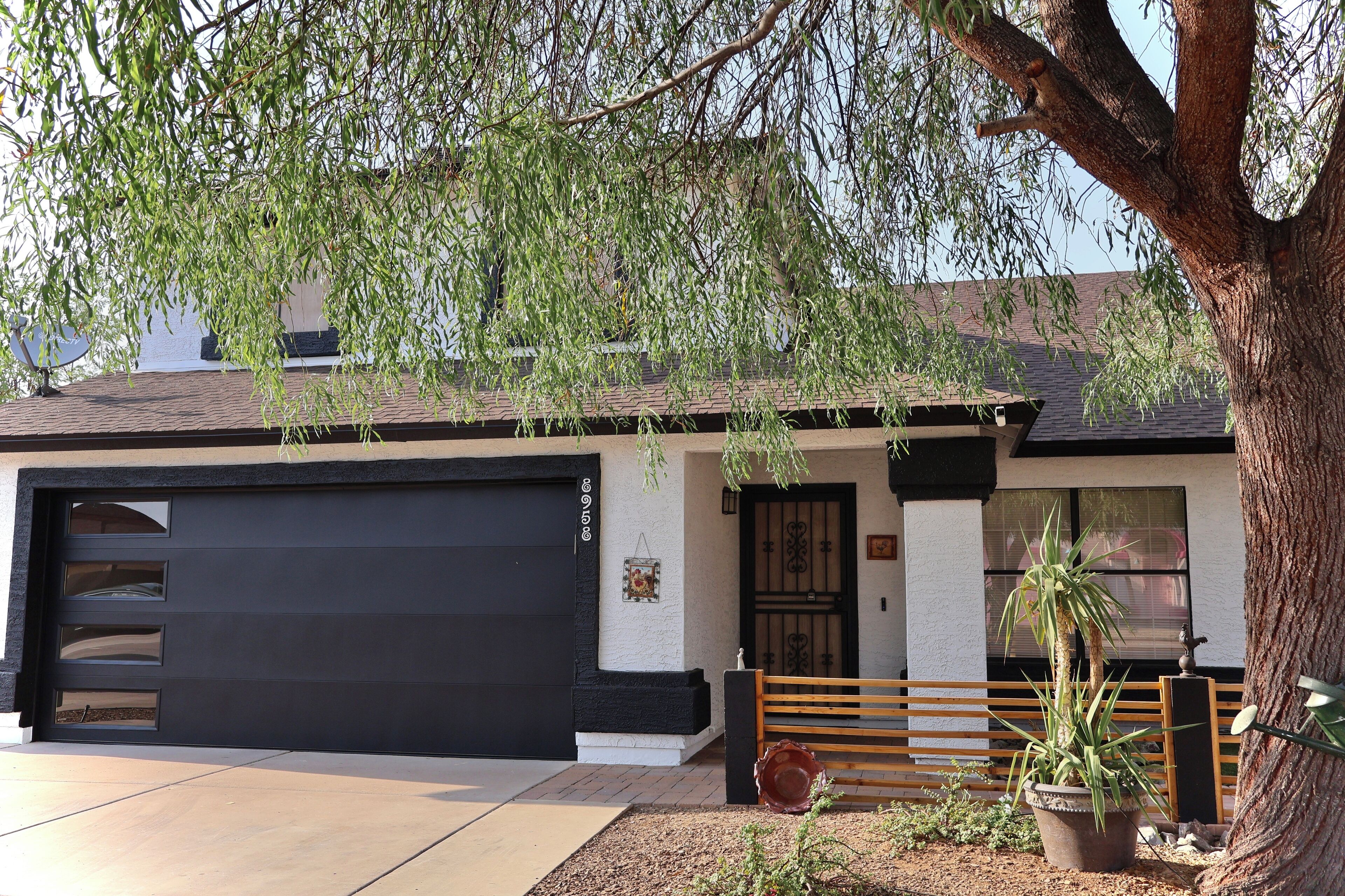 A residential building with a garage door, a wooden fence, and a large tree.