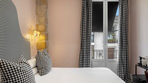 A hotel room with a bed, checkered curtains, a stone wall, and a balcony with potted plants. - Hotel Carmen Boutique (Úbeda)