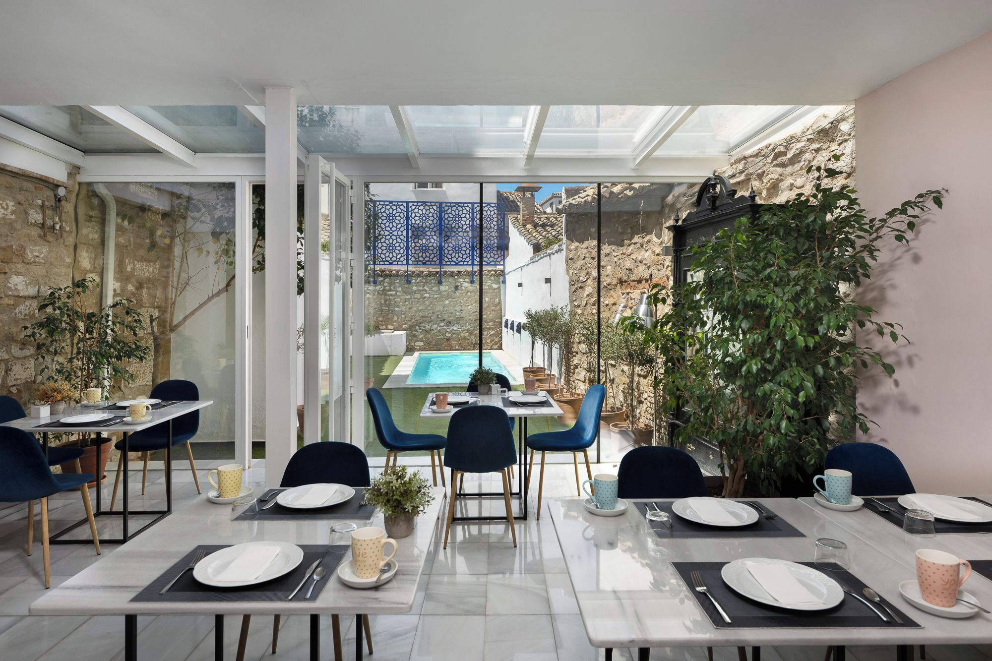 A dining area with tables set for four, a pool, and a view of a traditional courtyard.