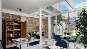 A dining area with a glass table, blue chairs, and a stone wall. - Hotel Carmen Boutique (Úbeda)