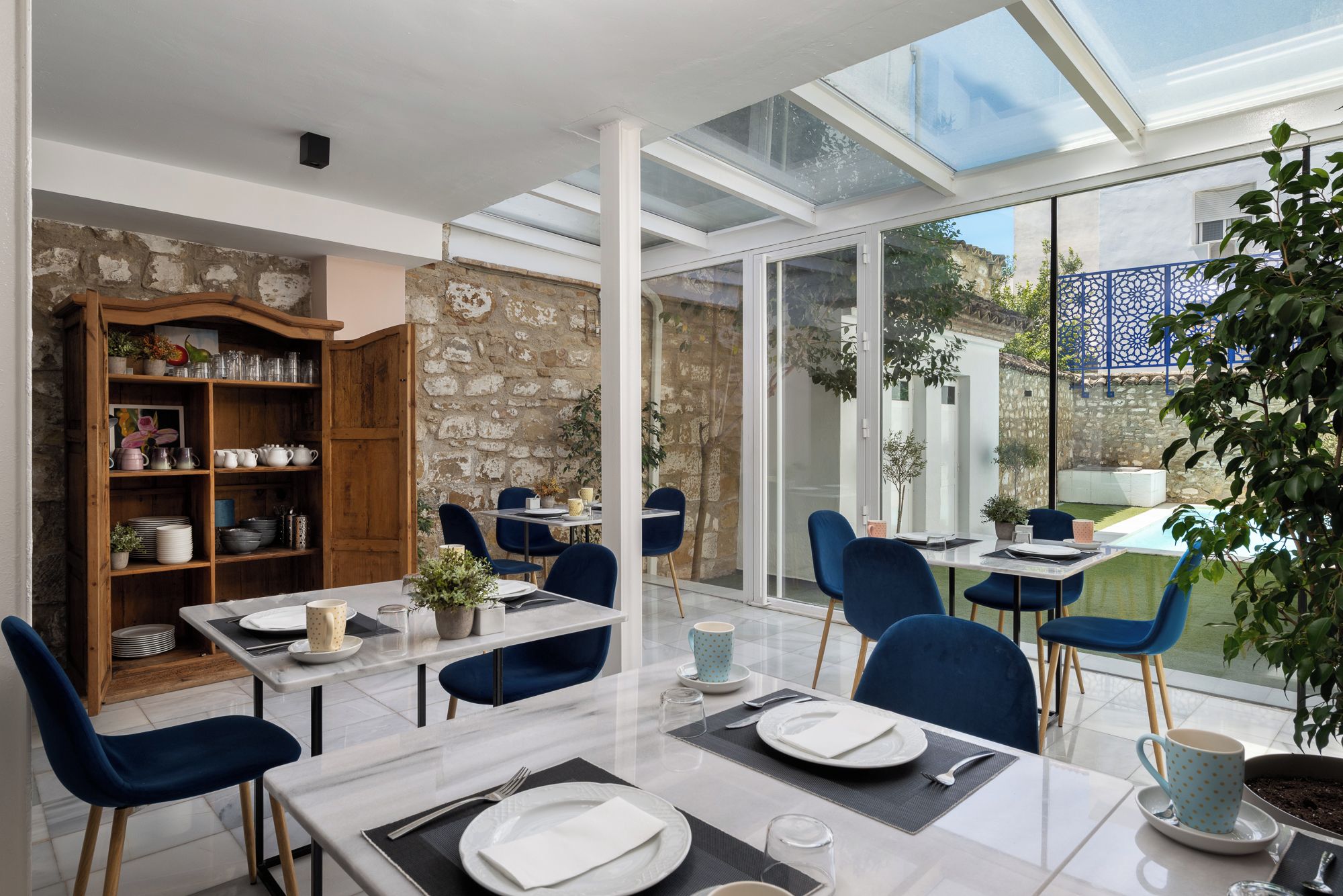 A dining area with a glass table, blue chairs, and a stone wall.