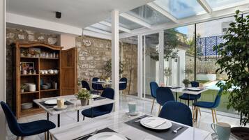 A dining area with a glass table, blue chairs, and a stone wall.