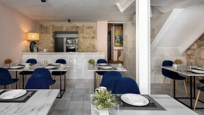 A dining area with marble tables, blue chairs, and a kitchen in the background. - Hotel Carmen Boutique (Úbeda)