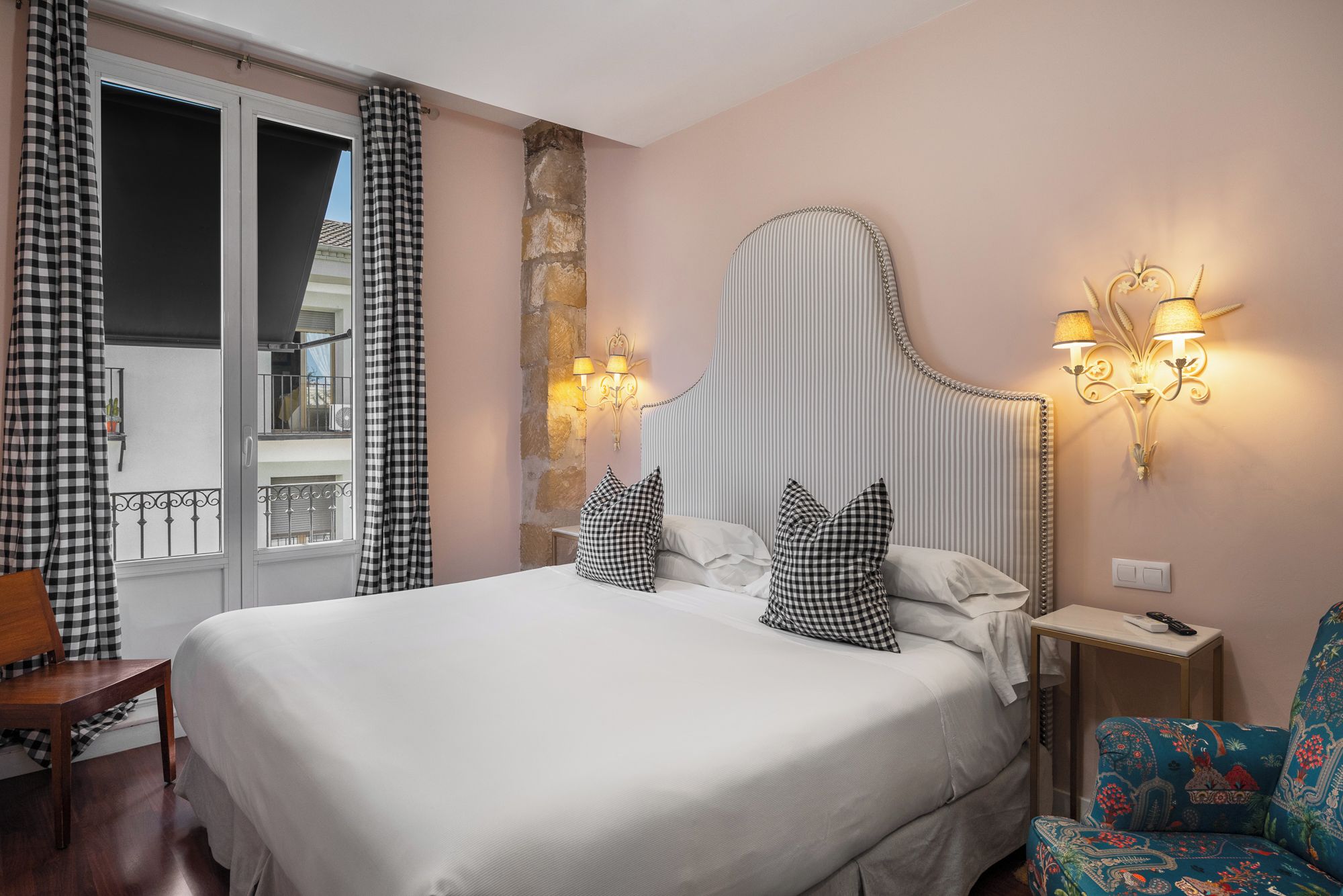 A hotel room with a large bed, checkered curtains, a stone accent wall, a decorative headboard, and wall-mounted lamps.