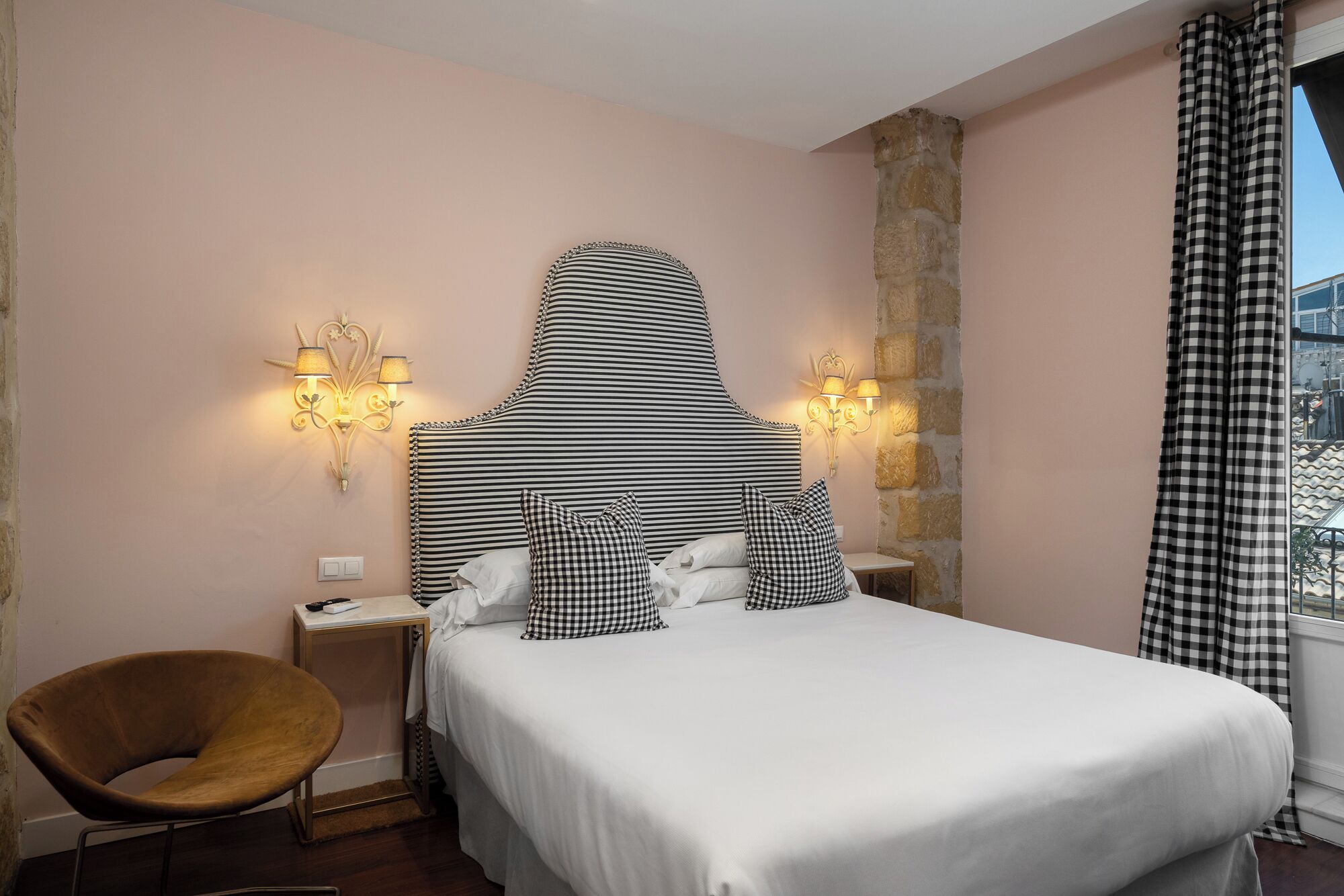 A hotel room with a bed, a chair, a nightstand, and two wall sconces.