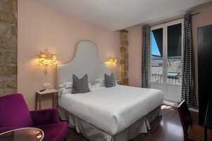 A hotel room with a bed, a chair, a nightstand, and a window with curtains.