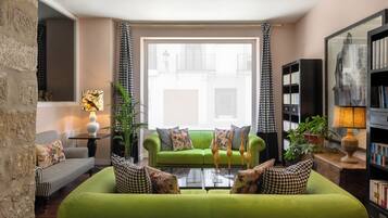 A living room with a green sofa, checkered pillows, a bookshelf, and a window with curtains.