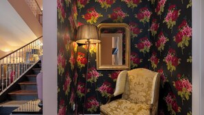 A staircase with a railing, a wall with floral wallpaper, a floor lamp, a mirror, and a patterned armchair. - Hotel Carmen Boutique (Úbeda)