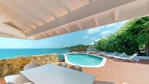 Zona de piscina exterior con vistas al mar, un porche cubierto y sillones de descanso.