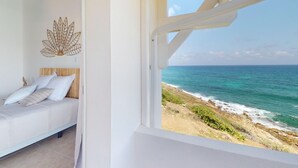 Un dormitorio con cama, un adorno en la pared y vista al océano a través de una ventana.