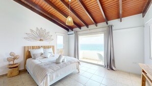Un dormitorio con una cama grande, vigas de madera en el techo, un adorno en la pared y vistas al mar.
