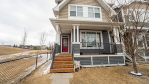 A two-story house with a red door, a front porch, and a small front yard. - Bright Auburn Bay Suite – Private, Furnished, Walk to South Health Campus (Calgary)