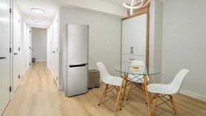 A modern kitchen with a glass dining table, white chairs, and a stainless steel refrigerator.