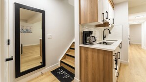 A modern kitchen with wooden cabinets, a black-framed mirror, and a coffee maker.