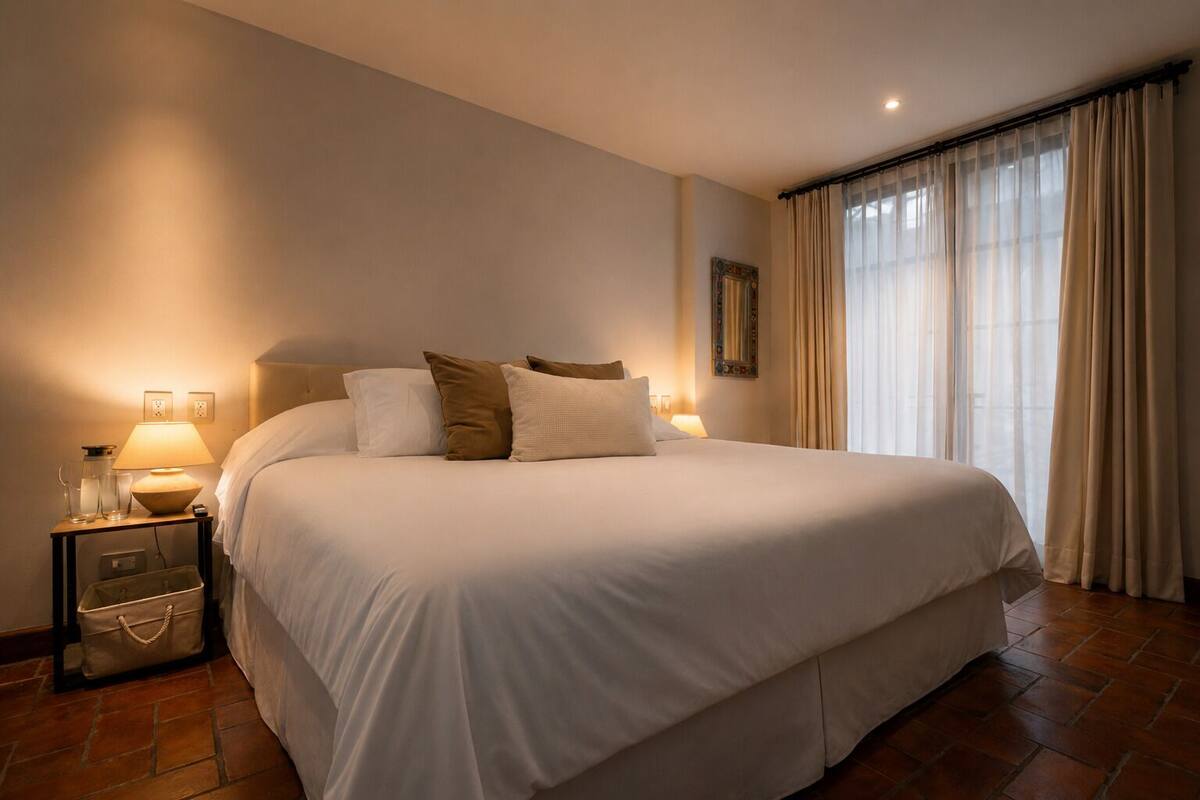 Une chambre d’hôtel avec un grand lit, des lampes de chevet, une table de nuit et une fenêtre avec des rideaux.