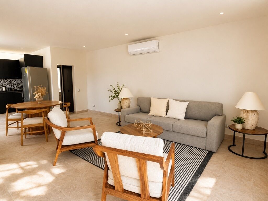 Een moderne woonkamer met een bank, twee fauteuils, een salontafel en een eethoek met stoelen en een tafel.