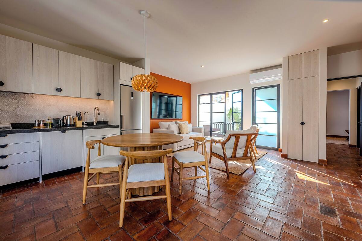 Une cuisine moderne avec un coin repas, comprenant un grand îlot central, des chaises en bois et un téléviseur fixé au mur.