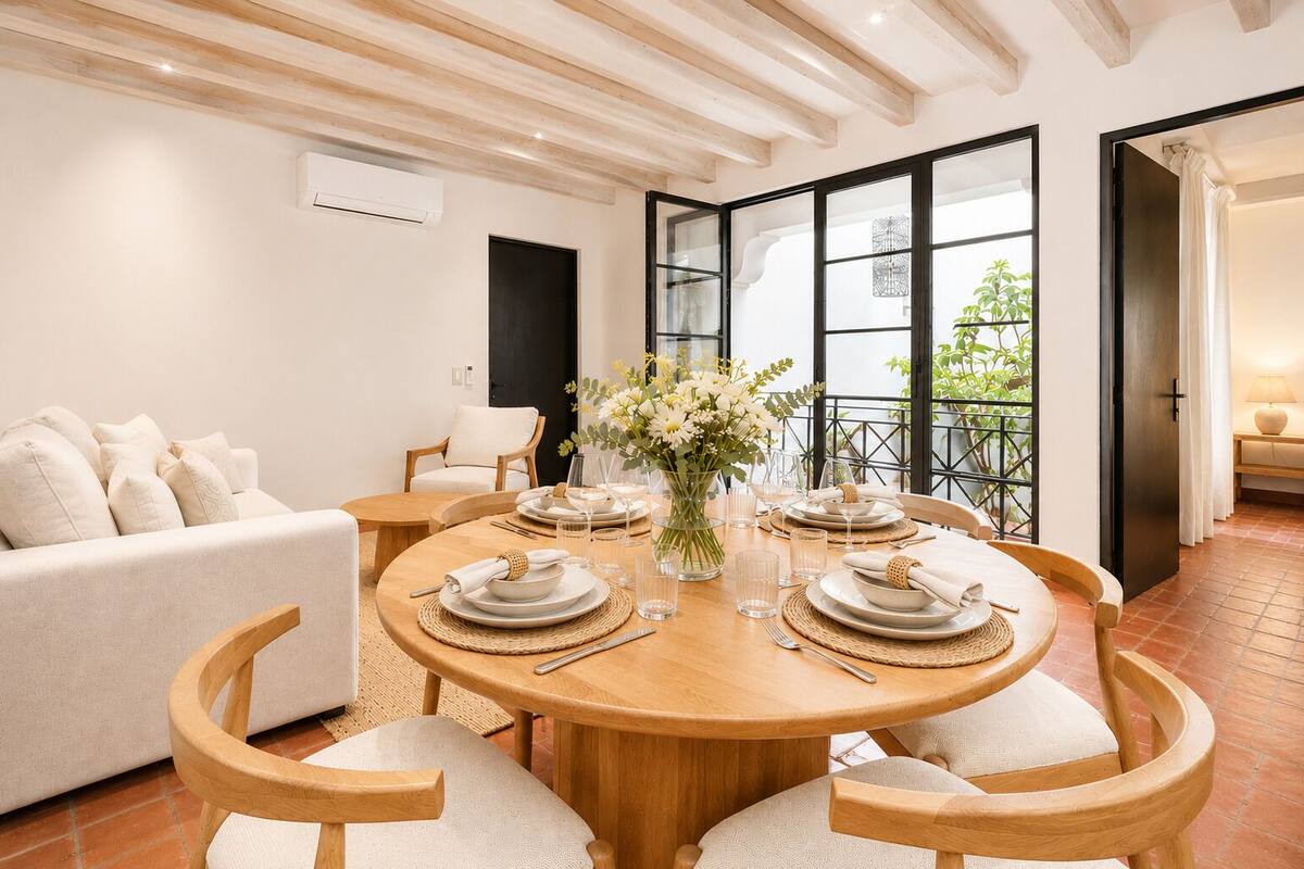 Un coin repas avec une table ronde en bois, dressée pour quatre personnes, entourée de chaises en bois.