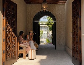 Un paseo techado con puertas de madera ornamentadas y vista a un edificio a través de un arco.