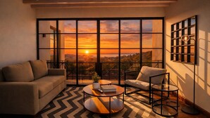 Una sala moderna con sofá, sillón, mesa de centro y un ventanal con vistas a la ciudad.