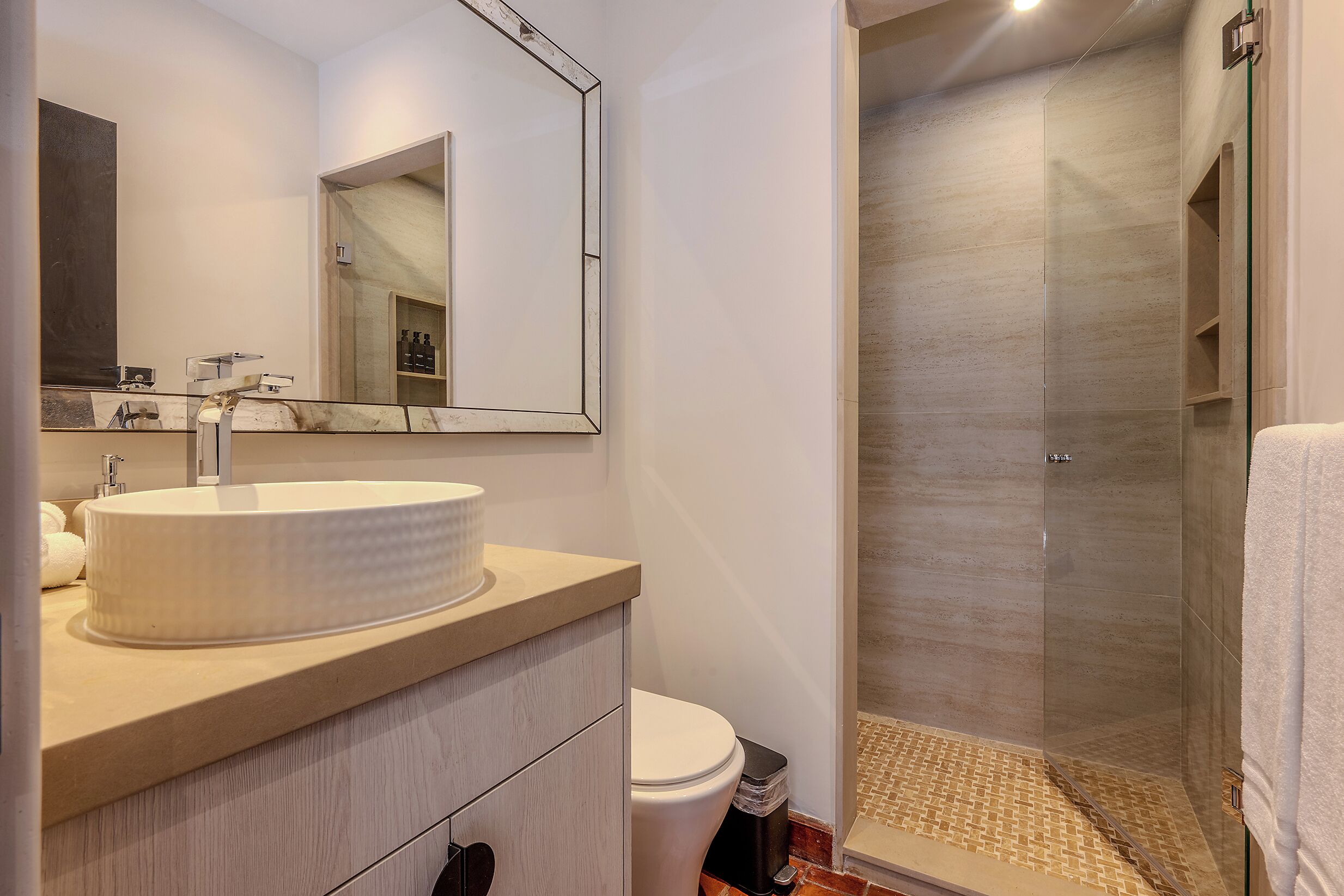 A bathroom with a large mirror, a round sink, a toilet, and a glass-enclosed shower area.