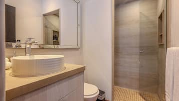 A bathroom with a large mirror, a round sink, a toilet, and a glass-enclosed shower area.