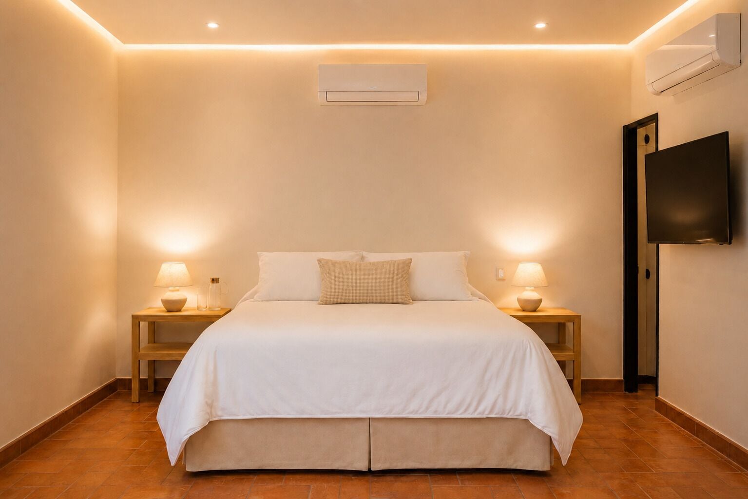 Habitación de hotel con cama, dos mesitas de noche con lámparas, un televisor de pantalla plana y un equipo de aire acondicionado.