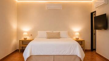 Habitación de hotel con cama, dos mesitas de noche con lámparas, un televisor de pantalla plana y un equipo de aire acondicionado.