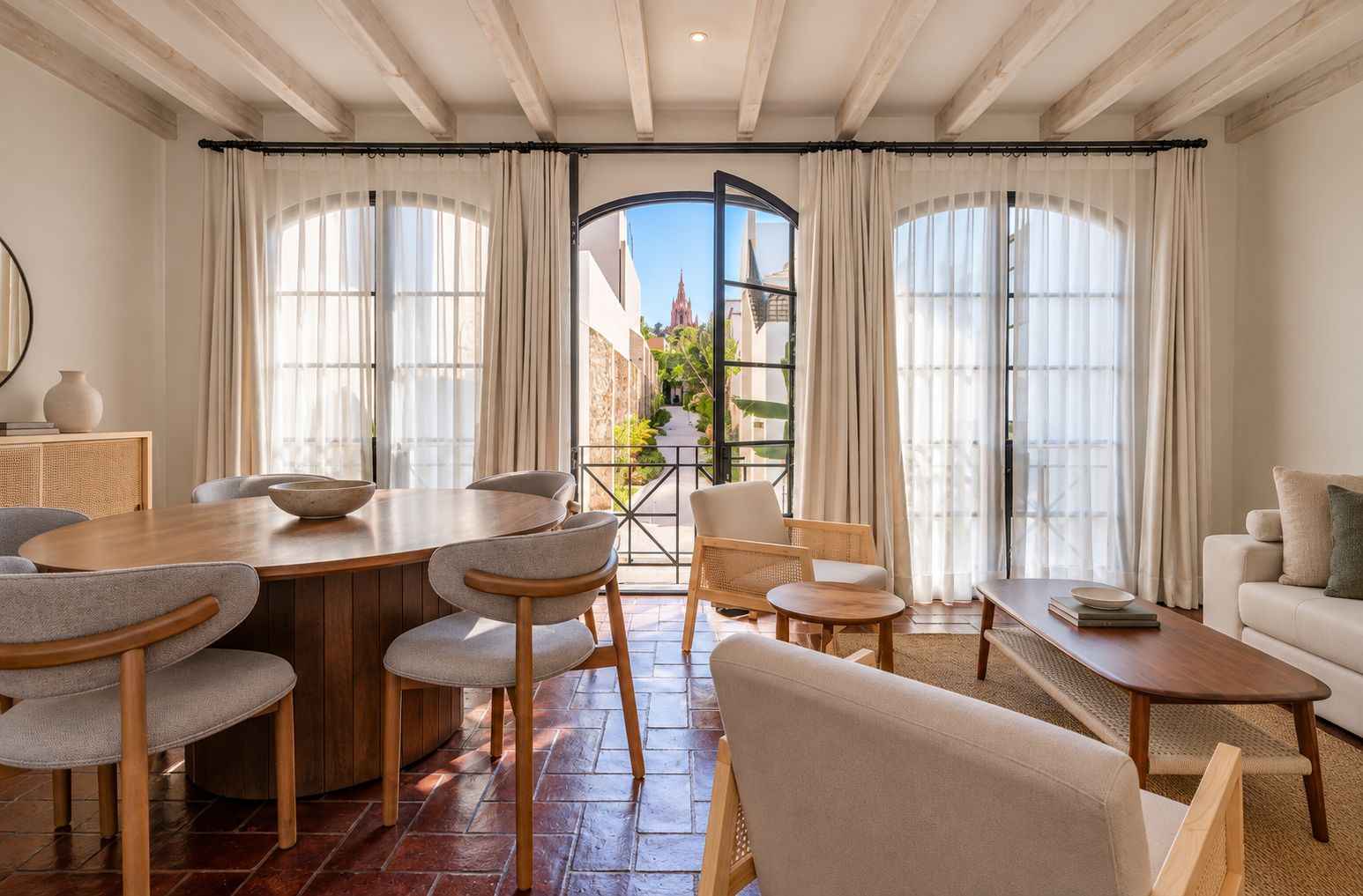 A spacious living area with a wooden dining table, comfortable seating, and large windows offering a view of the outside.