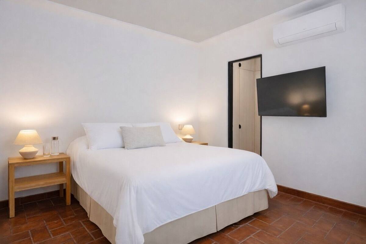 Une chambre à coucher comprenant un lit, deux tables de chevet avec des lampes, un téléviseur à écran plat et un appareil de climatisation fixé au mur.