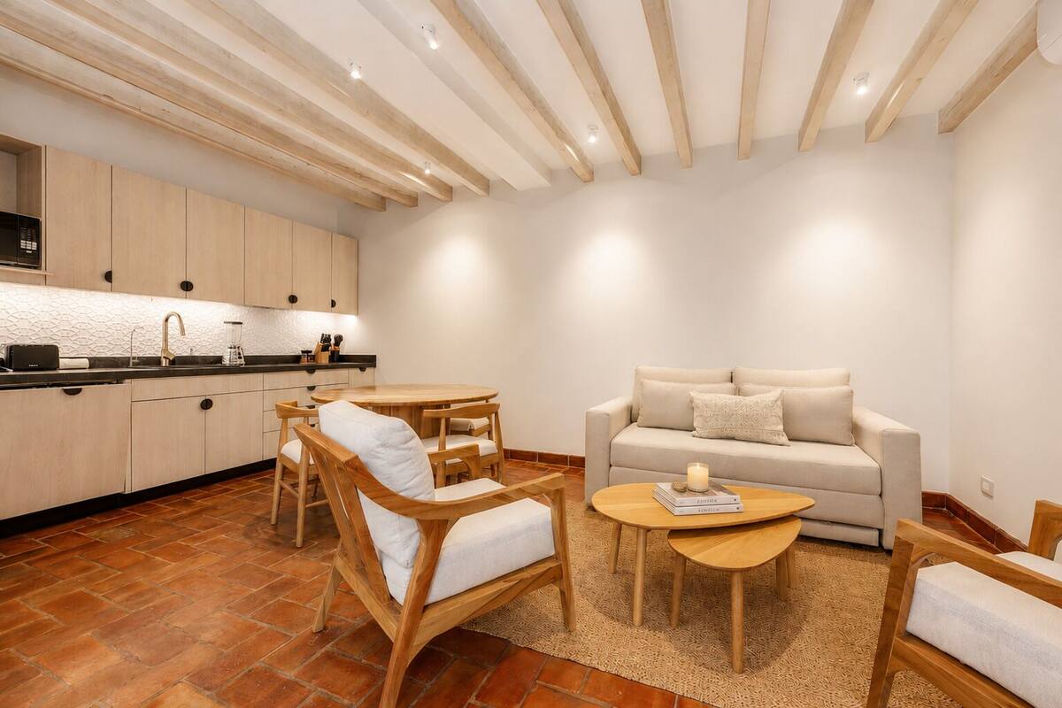 Un salon moderne comprenant un canapé, des fauteuils, une table basse et un coin cuisine avec des placards et des appareils électroménagers.