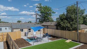 A backyard with artificial grass, a wooden fence, a blue shade sail, and a trampoline. - Finding Your Rhythm In The Heart Of It All (Colorado Springs)