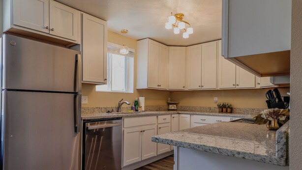 A modern kitchen with stainless steel appliances, white cabinetry, granite countertops, and a window with blinds. - Finding Your Rhythm In The Heart Of It All (Colorado Springs)
