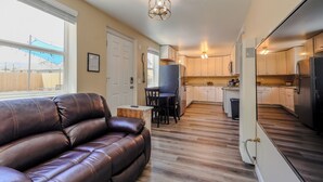 A modern kitchen with white cabinets, a dining area with a table and chairs, and a leather sofa in a living area with large windows. - Finding Your Rhythm In The Heart Of It All (Colorado Springs)