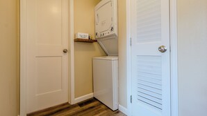 A laundry room with a washer and dryer, wooden flooring, and a shelf with a box. - Finding Your Rhythm In The Heart Of It All (Colorado Springs)