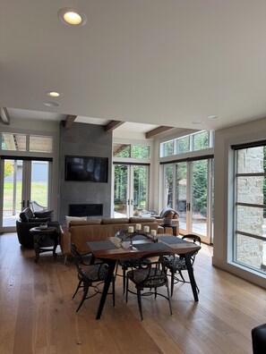 A spacious living area with a fireplace, large windows, and a dining table with chairs.