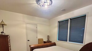A bedroom with a bed, a nightstand, a lamp, a dresser, and a window with blinds.