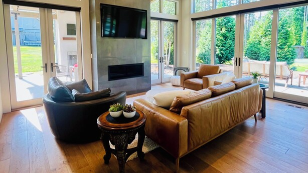 A spacious living room with a fireplace, leather sofas, and large windows offering a view of the outdoors.