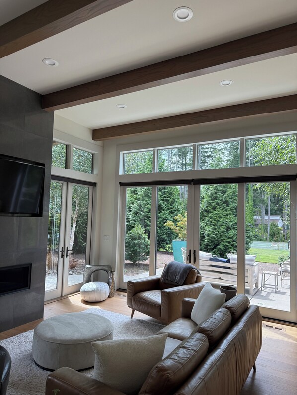 A spacious living room with a large sectional sofa, ottoman, and a flat-screen TV mounted on the wall.