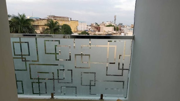 Un balcone con una parete divisoria in vetro a motivi geometrici, una sedia in legno e vista su un paesaggio urbano con edifici e palme.