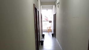 Un corridoio stretto, rivestito di piastrelle, con porte su entrambi i lati, che conduce a una zona con balcone, una sedia e un cestino.