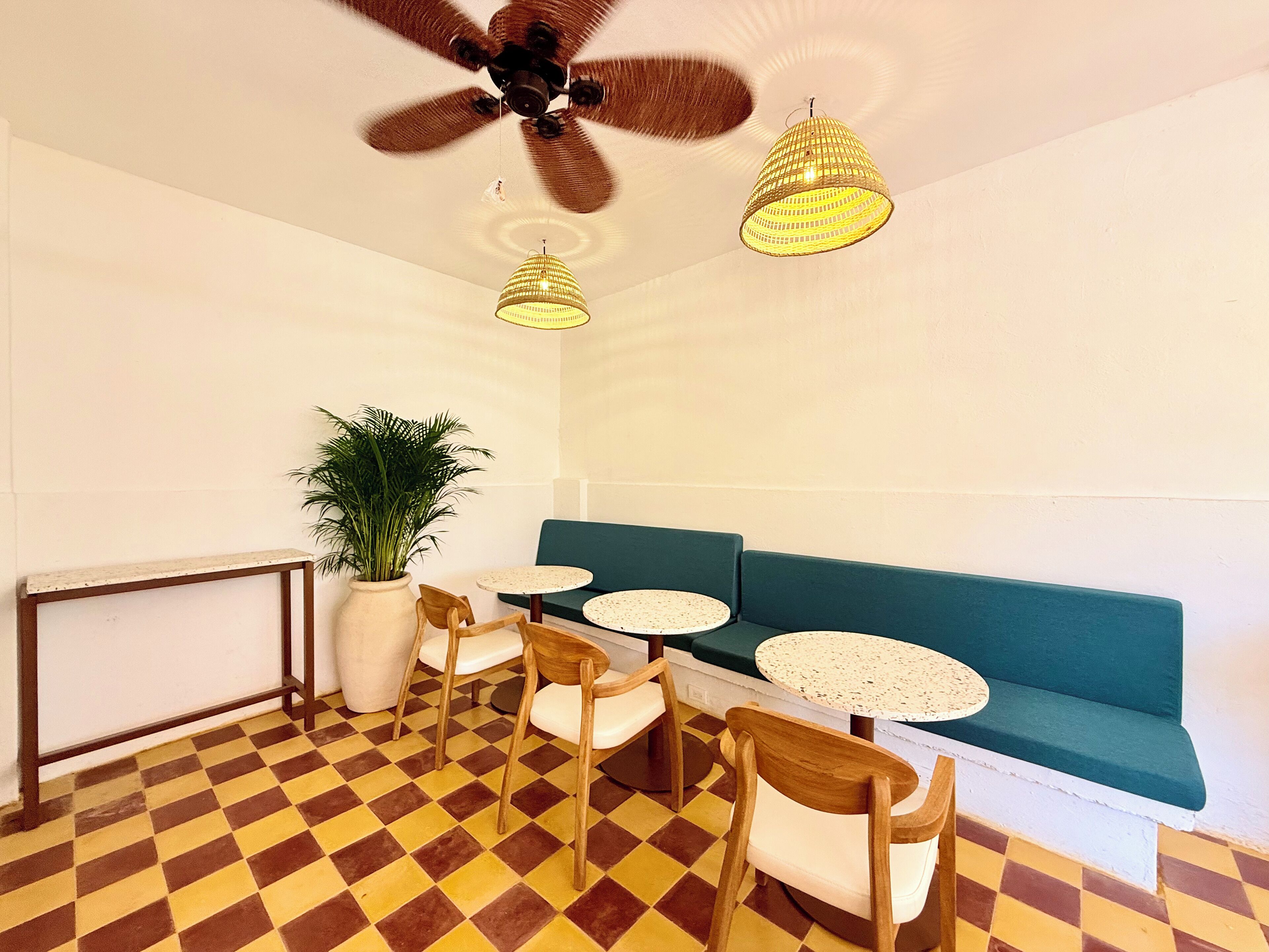 A room with a checkered floor, a green sofa, wooden chairs, a white table, a potted plant, and a ceiling fan.