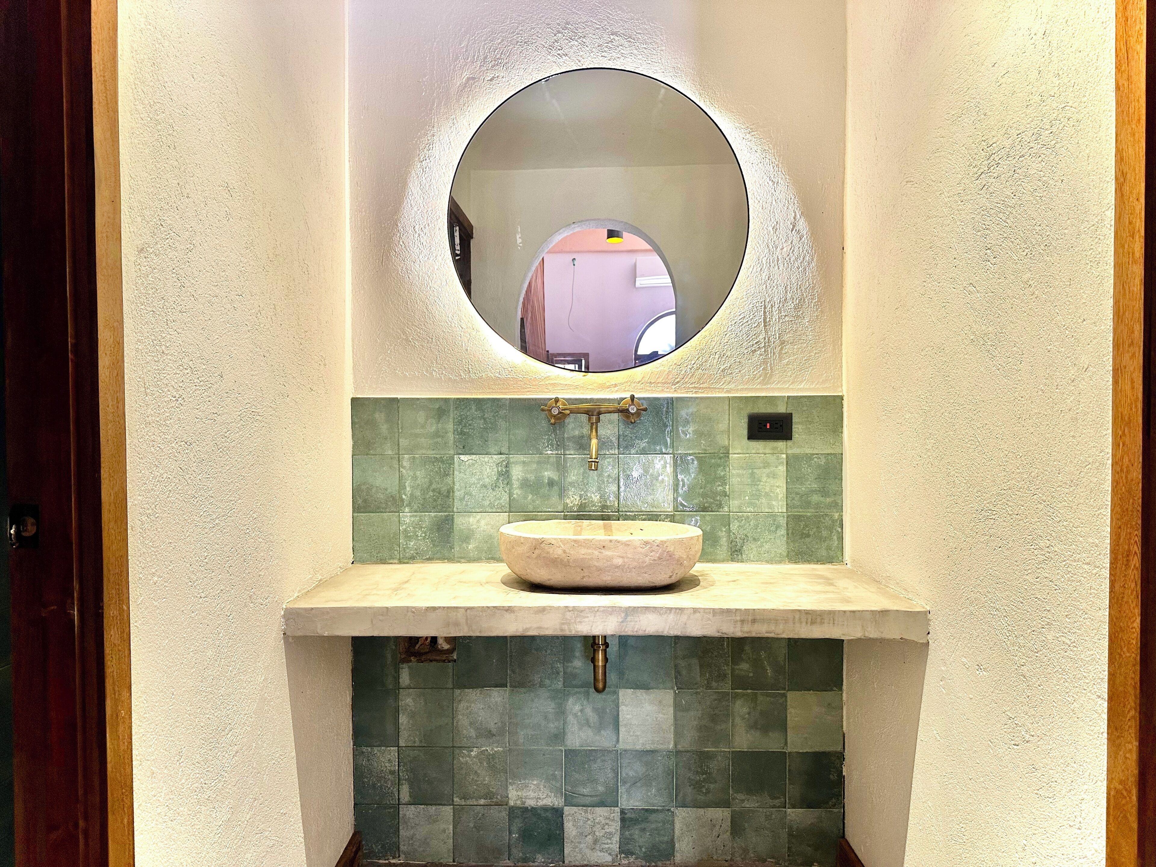 Une salle de bain avec un miroir rond, un lavabo et des murs recouverts de carreaux verts.