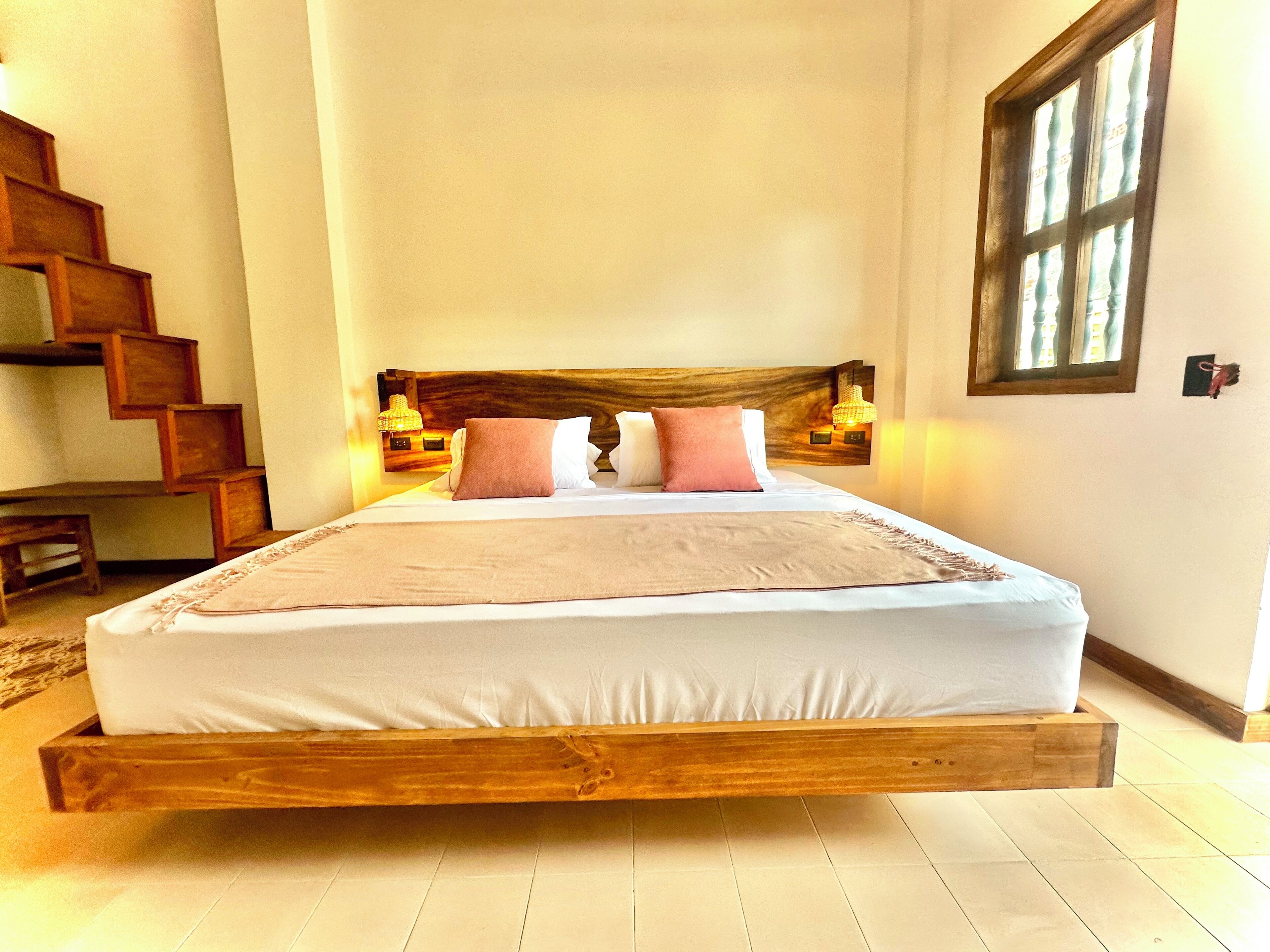 Una cama con estructura de madera, dos almohadas y una lámpara de noche.