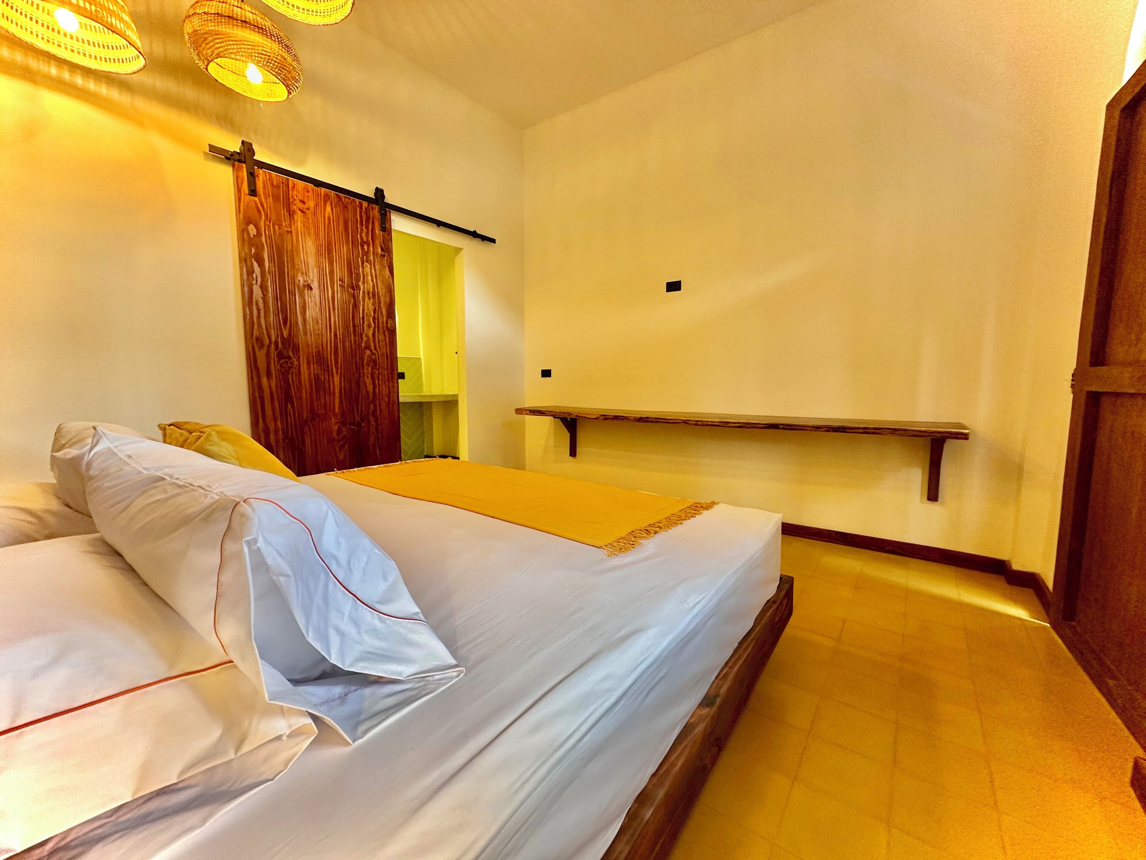 Un dormitorio con cama, armario de madera, lámpara colgante y pequeña estantería de madera.