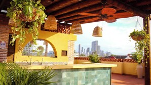A rooftop bar with hanging plants, a large window, and a city skyline view.