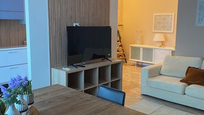 A modern living room with a wooden dining table, a flat-screen TV, and a white sofa. - Apartment near american school from the center of milan from IEO and Humanitas (Noverasco)