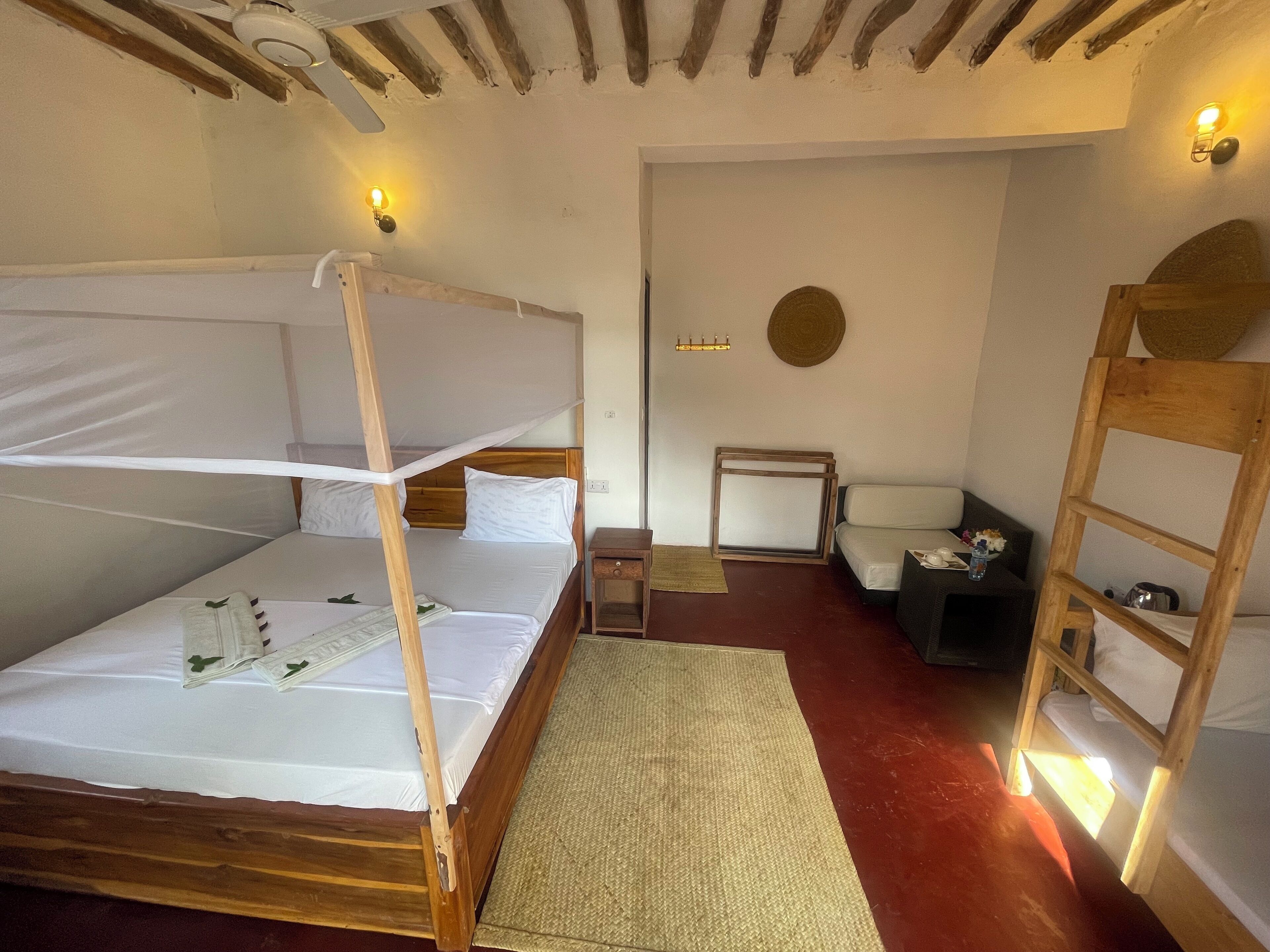 A room with a wooden bunk bed, a small table with a lamp, a chair, and a ladder.