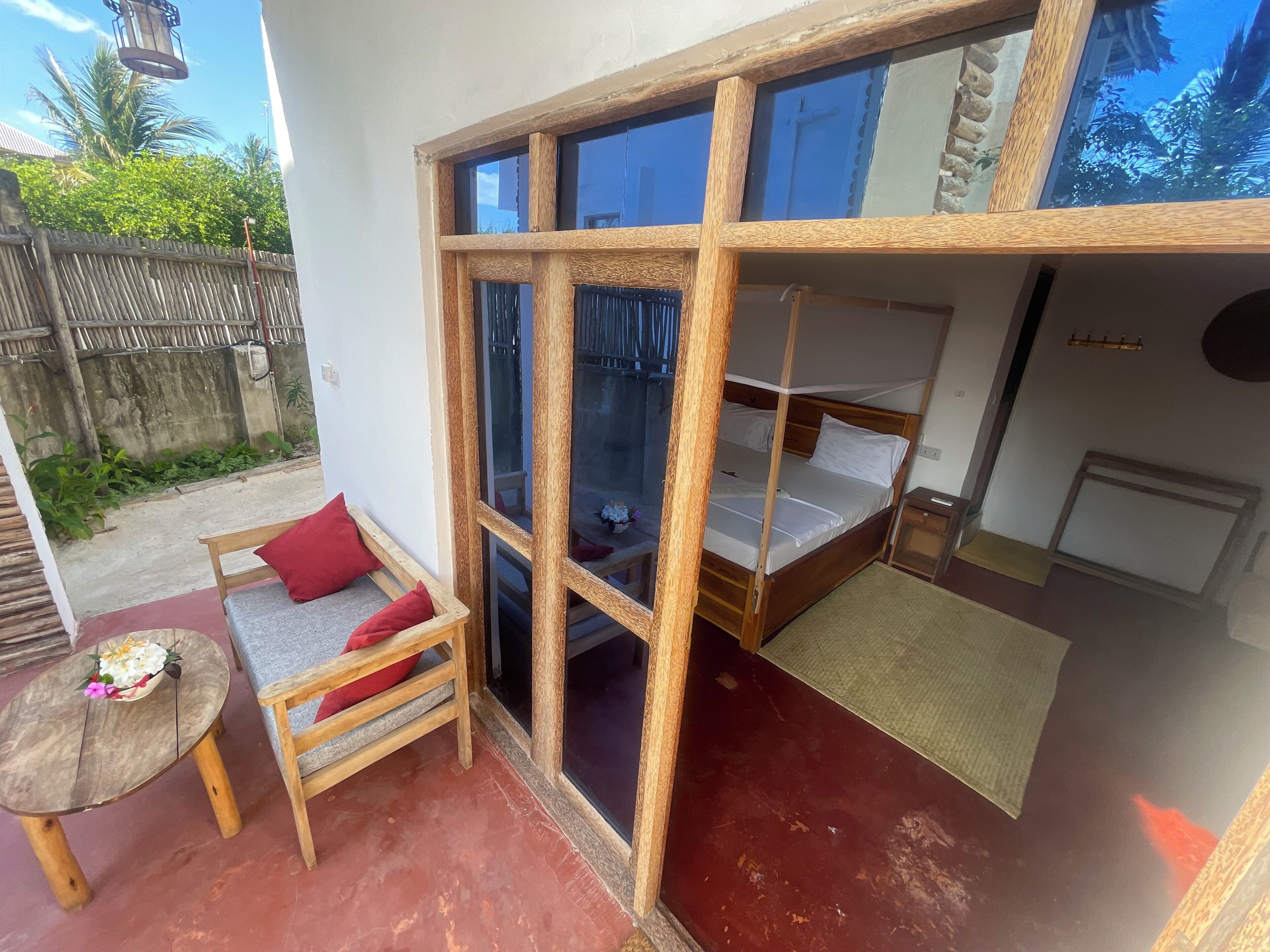 Una habitación con una cama litera de madera, un pequeño rincón de descanso con un banco y cojines, y una mesa con un arreglo floral.