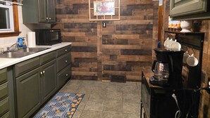 A kitchen with wooden panel walls, green cabinets, a microwave, a coffee maker, and a framed picture on the wall. - Charming Cape Cod minutes from YSU, Covelli Center and many more! Pet Friendly (Youngstown)